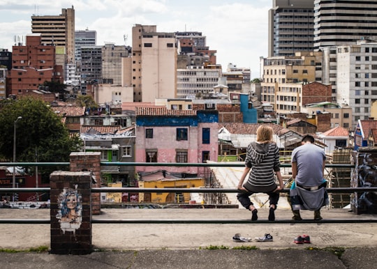 photo of two people sitting on pole fence facing high-rise building in Bogota Colombia