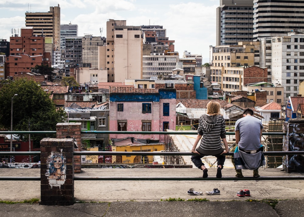 Foto de dos personas sentadas en la valla de postes frente a un edificio de gran altura