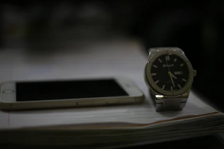 A sleek black and gold watch resting beside a smartphone displaying a WhatsApp chat screen.
