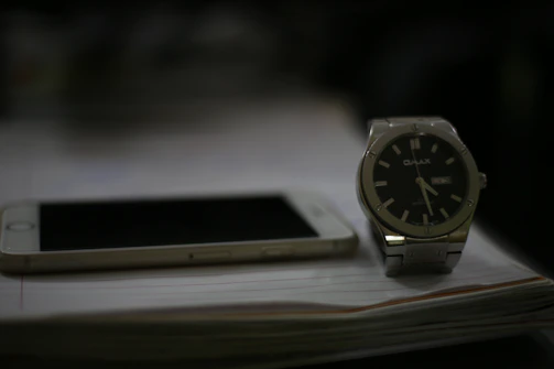 A sleek black and gold watch resting beside a smartphone displaying a WhatsApp chat screen.
