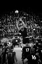 Close-up of a rugby ball on the field with cheering crowd blurred in background.