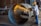 A worker wearing a hard hat and protective gear uses an angle grinder to cut through a large metal pipe. Bright sparks are emitted from the cutting process, creating a vivid contrast against the industrial setting. In the background, there are various tools and equipment characteristic of a workshop environment.