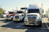 A semi truck fleet lined up at a depot with drivers checking their electronic devices.
