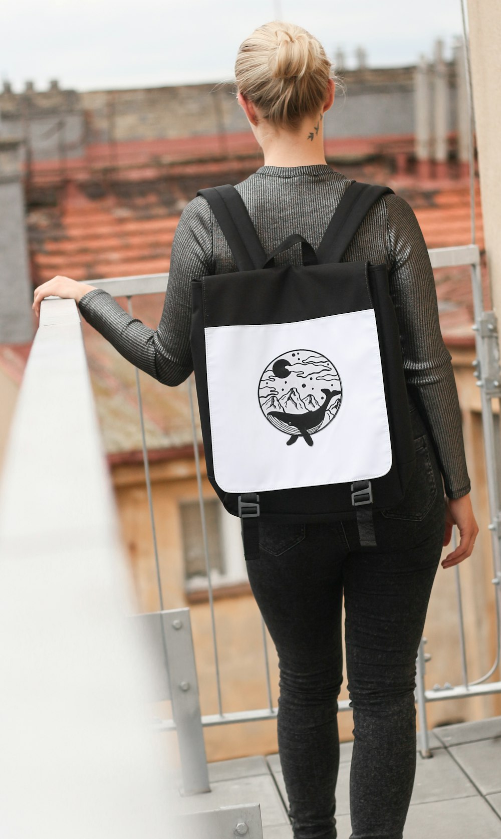 手すりを持ちながらテラスに立つ白黒のバックパックを背負った女性のセレクティブフォーカス写真