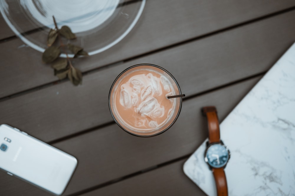 glass of beverage beside smartphone