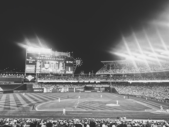 A bowler delivering a fast ball under bright stadium lights with an intense crowd in the background.