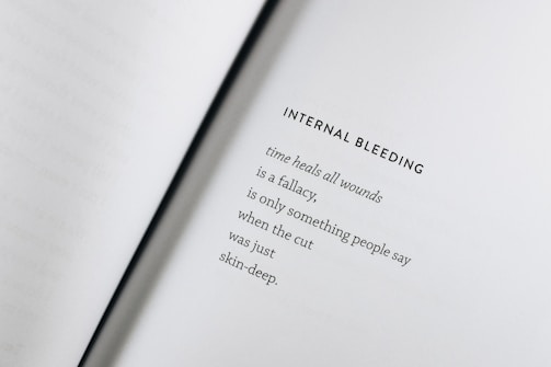 An open book with a poem titled 'Internal Bleeding' written on the right page. The text is centered and the page is mostly blank except for the poem, which discusses the concept that 'time heals all wounds' is a fallacy.