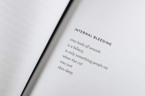 An open book with a poem titled 'Internal Bleeding' written on the right page. The text is centered and the page is mostly blank except for the poem, which discusses the concept that 'time heals all wounds' is a fallacy.