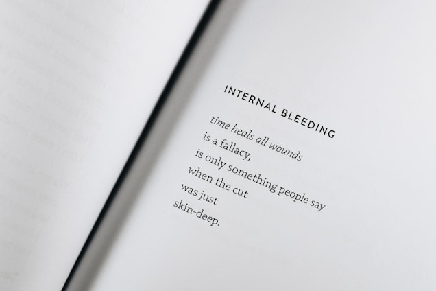 An open book with a poem titled 'Internal Bleeding' written on the right page. The text is centered and the page is mostly blank except for the poem, which discusses the concept that 'time heals all wounds' is a fallacy.