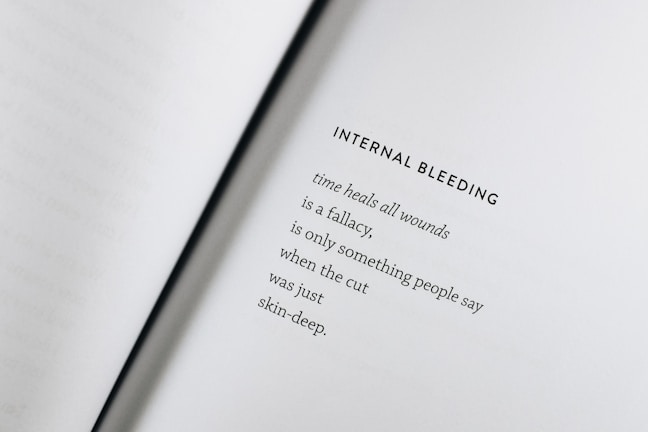 An open book with a poem titled 'Internal Bleeding' written on the right page. The text is centered and the page is mostly blank except for the poem, which discusses the concept that 'time heals all wounds' is a fallacy.