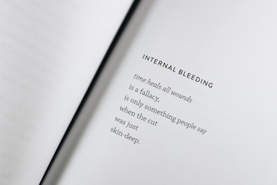 An open book with a poem titled 'Internal Bleeding' written on the right page. The text is centered and the page is mostly blank except for the poem, which discusses the concept that 'time heals all wounds' is a fallacy.