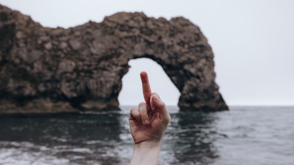 person showing right middle finger on front of brown rock formation