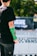 A person with a green cast on their arm is standing outdoors. The background displays a blurred event banner with a Vans logo, suggesting a skateboarding or sports-related event. The person wears a black t-shirt and pants, and there is a focus on their injured arm.