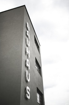 A tall, minimalist building with the word 'BAUHAUS' displayed vertically on its facade. The structure features sleek, clean lines and a few windows with a modernist design.