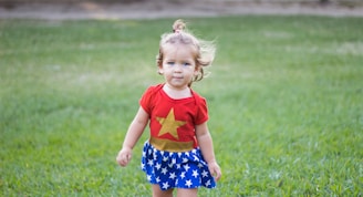 girl wearing Wonder Woman dress walking on green grass field during daytime