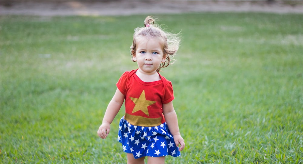 menina vestindo o vestido da Mulher-Maravilha andando no campo de grama verde durante o dia