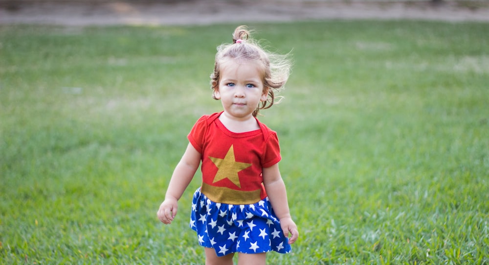 girl wearing Wonder Woman dress walking on green grass field during daytime