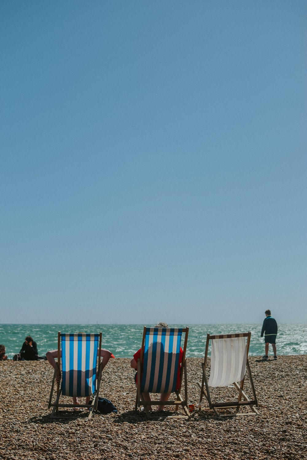 two person sitting on blue striped folding chairs near body of water