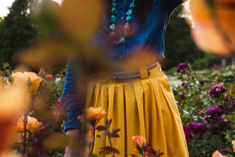 woman in yellow skirt and blue shirt standing on bed of flowers