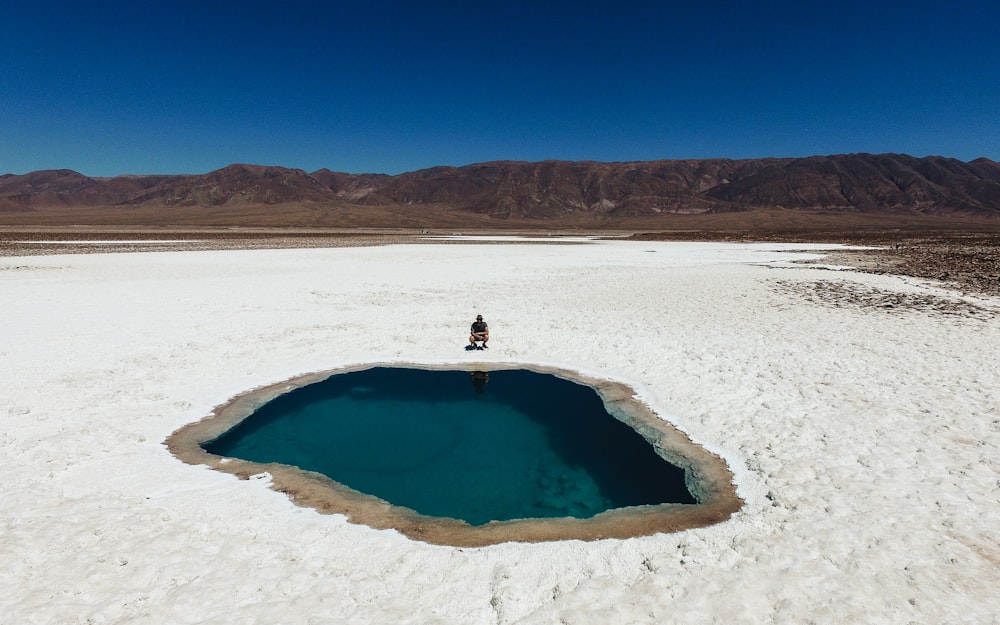 person wearing black shirt sitting near blue hole under blue sky during daytime