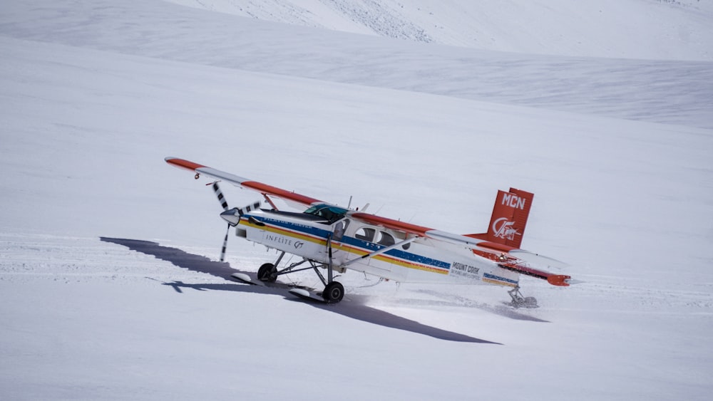 photo of white, blue, and red plane on white snow at daytime