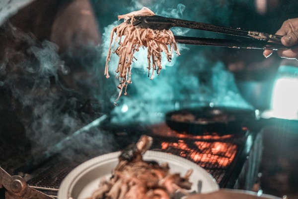 person holding black thong with grilled food in front of person holding white ceramic plate filled with grilled food