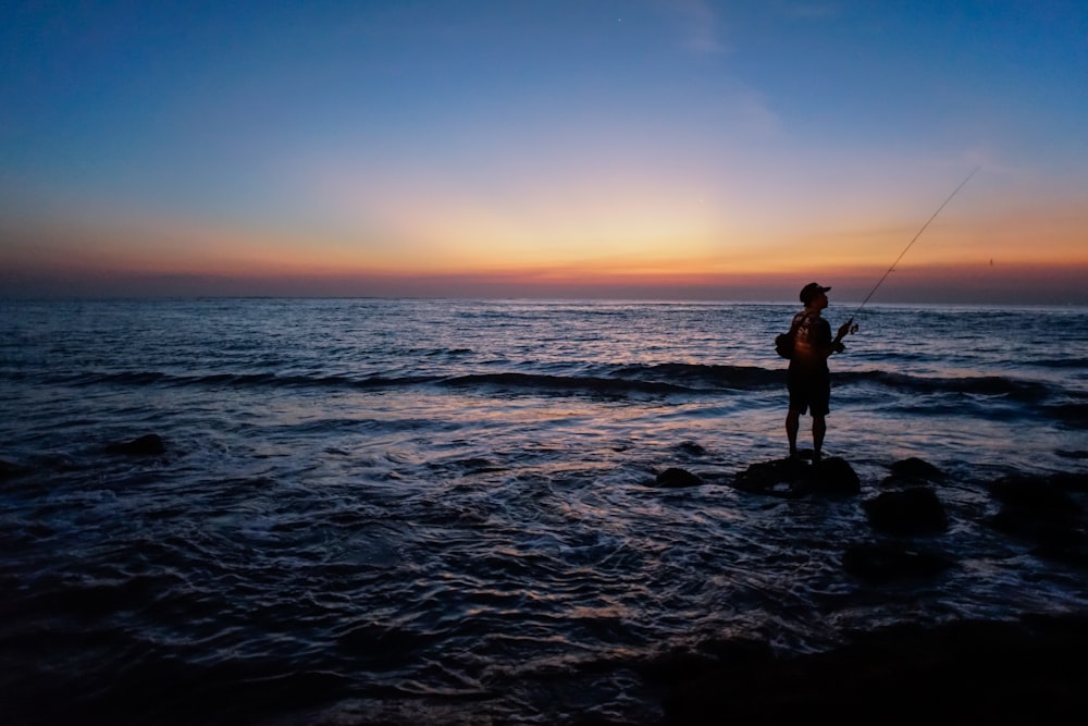 Mann fischt am Meeresufer während der goldenen Stunde