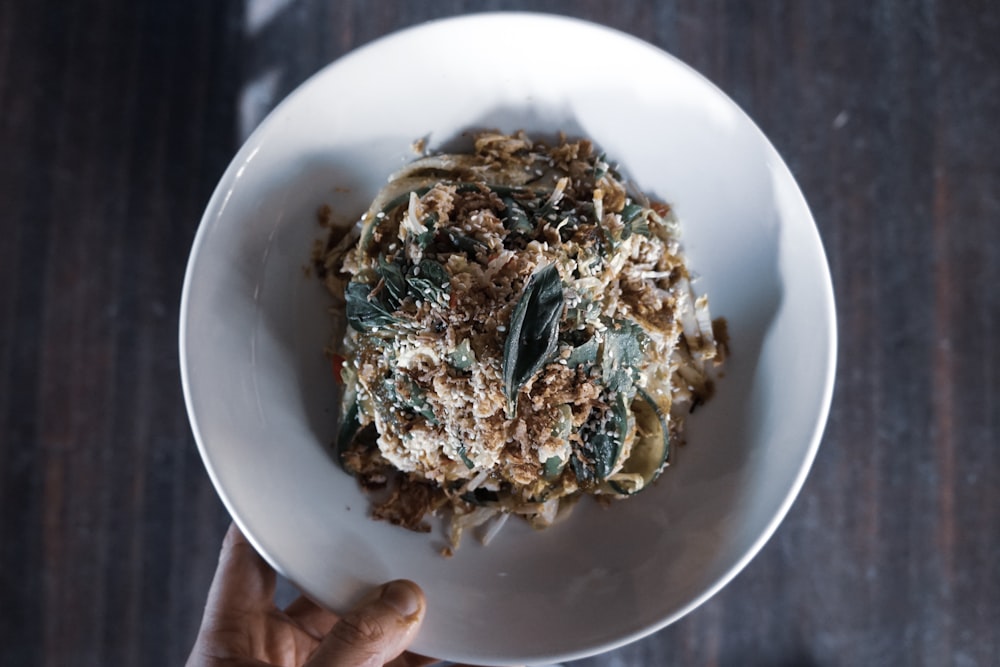 person holding white bowl with meat salad