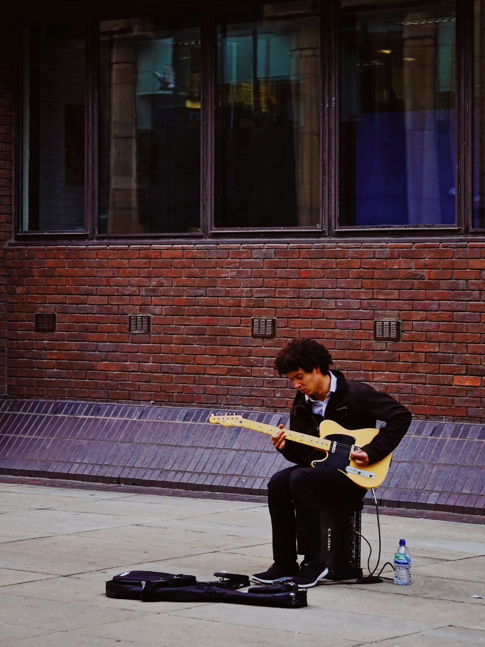 Mann, der mit seiner E-Gitarre spielt, während er auf dem Gitarrenverstärker sitzt
