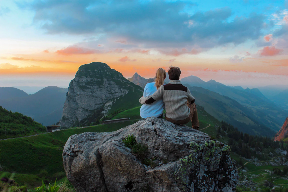 A couple sitting together on a rock, looking out over a mountain view