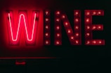 Bright neon sign displaying the word 'WINE' against a dark background. Each letter is illuminated with vibrant red lights, creating a striking contrast with the surrounding darkness.