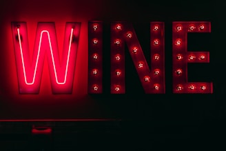 Bright neon sign displaying the word 'WINE' against a dark background. Each letter is illuminated with vibrant red lights, creating a striking contrast with the surrounding darkness.