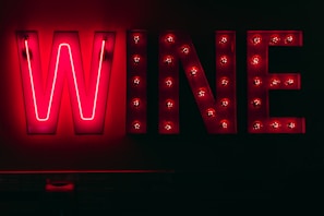 Bright neon sign displaying the word 'WINE' against a dark background. Each letter is illuminated with vibrant red lights, creating a striking contrast with the surrounding darkness.