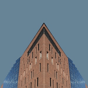A modern building with a triangular corner, featuring a facade of brown brick and blue glass. The architecture showcases a blend of contemporary design elements with straight lines and reflective surfaces, under a clear sky.