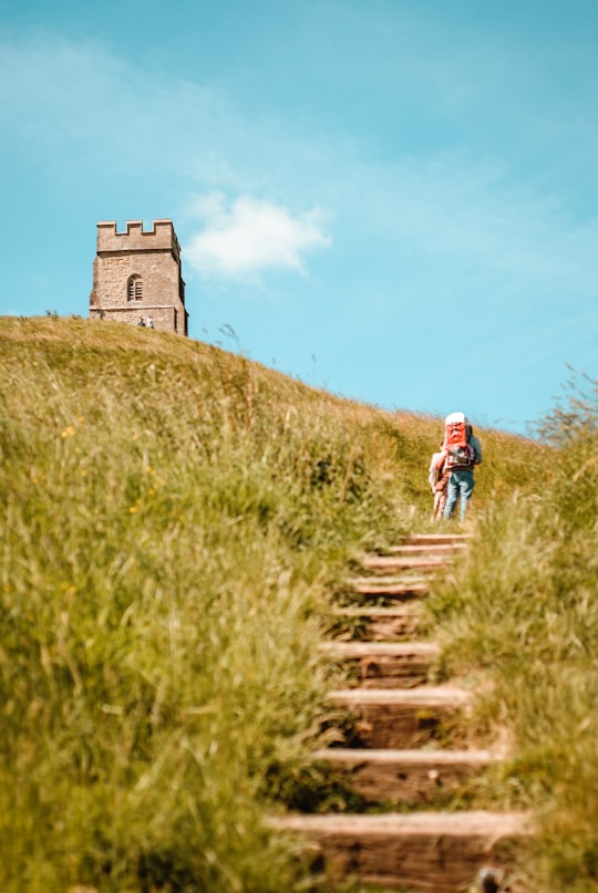 two person walks on hills near concrete stucture in Glastonbury Tor United Kingdom