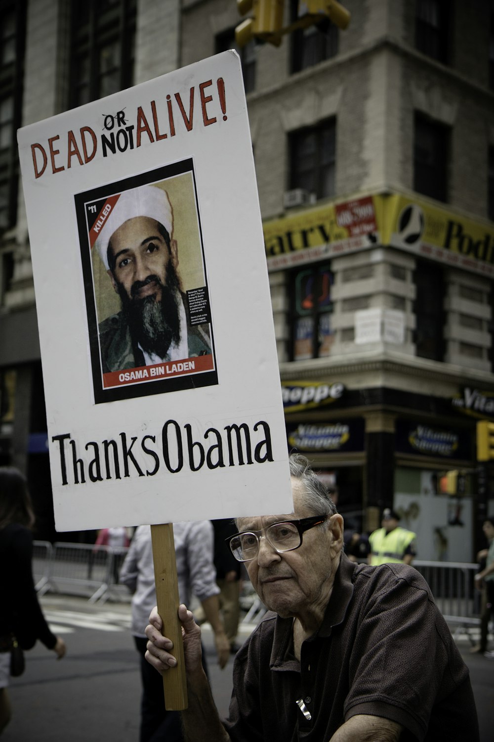 homem sentado segurando Dead Not Alive! Obrigado Obama placard