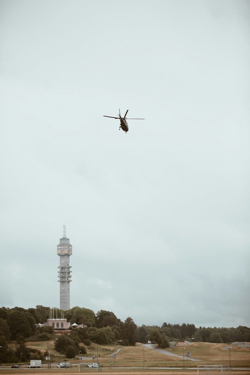 Photographie en contre-plongée d’un hélicoptère noir au-dessus d’une tour en béton gris pendant la journée