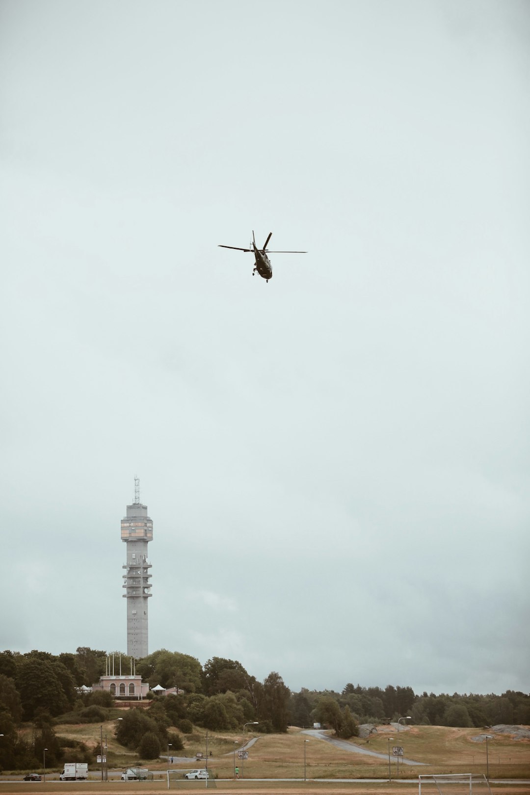 low-angle photography of black helicopter over gray concrete tower during daytime