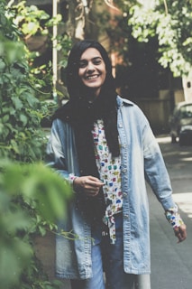 A model wearing a trendy jacket and jeans, smiling outdoors on a sunny day