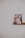 A framed photograph is placed on a simple wooden shelf. The image within the frame shows a person with intricate floral headpieces and face paint, featuring soft pastel colors. The background is a plain, light-colored wall that enhances the minimalistic and artistic presentation.
