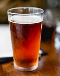 beverage filled clear pint glass on top of brown surface