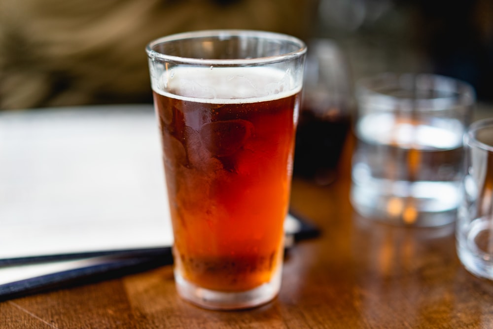 beverage filled clear pint glass on top of brown surface