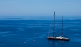 A large, elegant sailboat is anchored on a calm, deep blue sea. The horizon blends softly into the sky, creating a serene and expansive ocean scene. Small kayaks or canoes can be seen near the sailboat, adding a sense of exploration and adventure.