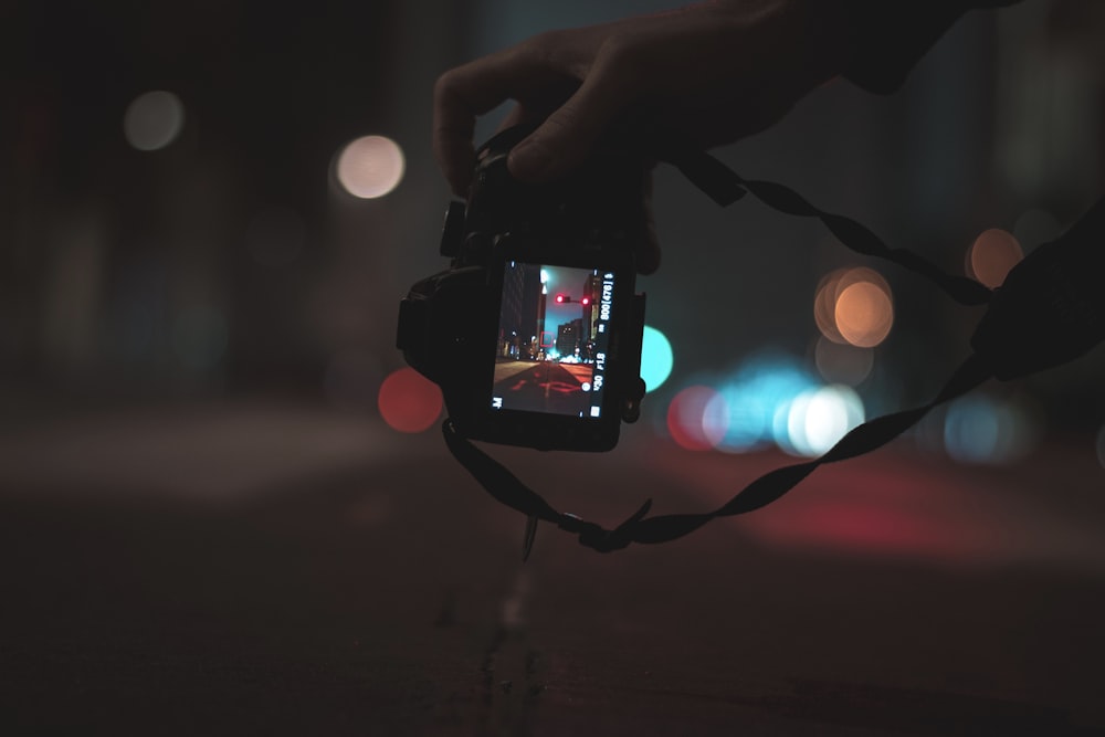 person holding black DSLR camera capturing photo of streets with bokeh lights