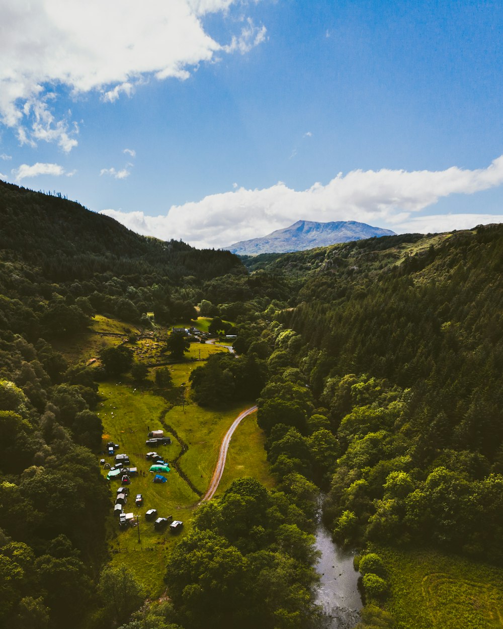 forested mountain with camp ground and river under blue sky and white clouds during daytime