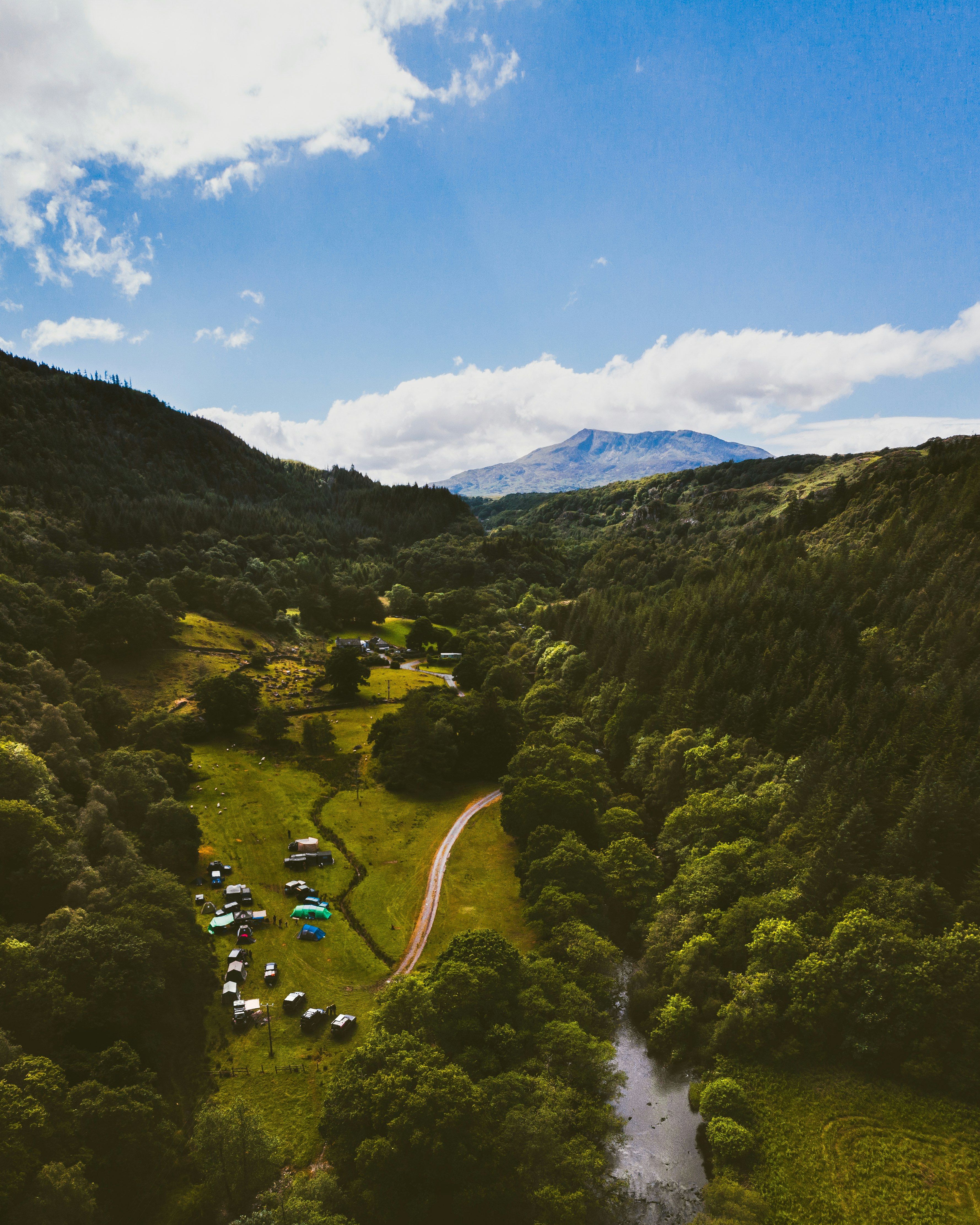 forested mountain with camp ground and river under blue sky and white clouds during daytime