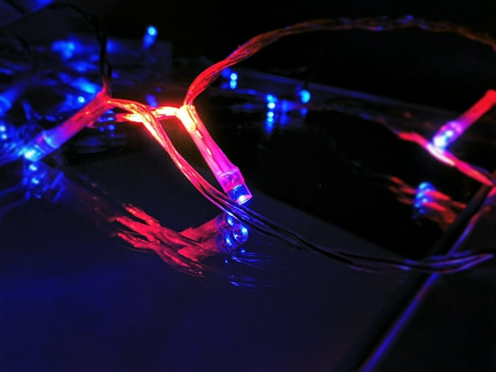 A string of decorative LED lights emitting red and blue light. The lights are intertwined, creating a vibrant and dynamic visual effect against a dark background. The glow of the lights reflects off the nearby surfaces, enhancing the vivid colors.