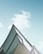 A modern architectural structure with sharp, angular lines and a reflective glass surface set against a bright blue sky with soft clouds.