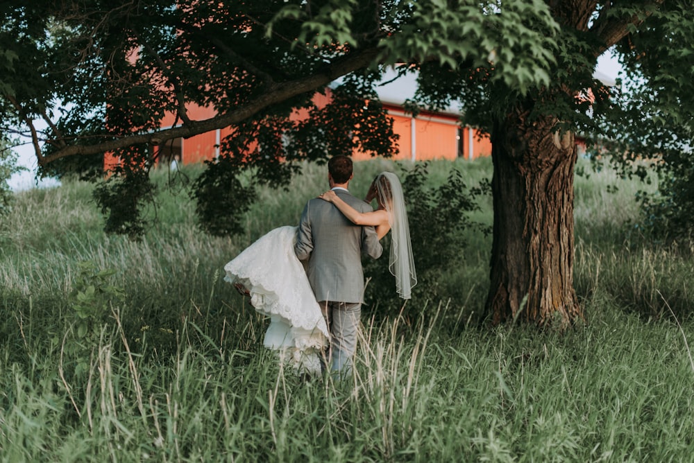 Ehemann trägt seine Frau, die neben Bäumen geht
