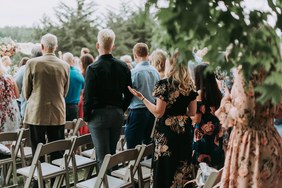 Invités élégamment habillés debout lors d'une cérémonie de mariage en extérieur